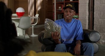 Movie still from “Half Baked” (1998), directed by Tamra Davis – A man sitting on the floor holding a bag of marijuana; Medium shot, Overhead angle
