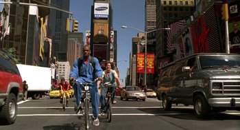 Movie still from “Half Baked” (1998), directed by Tamra Davis – A group of people riding bikes down a street; Wide shot, Low angle