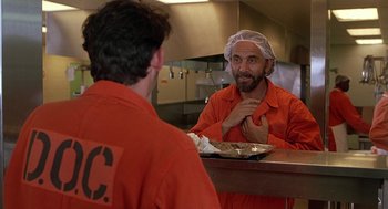 Movie still from “Half Baked” (1998), directed by Tamra Davis – A man in a red jumpsuit is sitting at a table; Medium shot, Over the shoulder angle