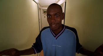 Movie still from “Half Baked” (1998), directed by Tamra Davis – A man in a blue and black shirt is smiling; Medium shot, High angle