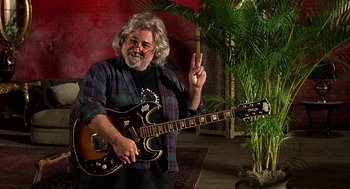 Movie still from “Half Baked” (1998), directed by Tamra Davis – A man holding a guitar and making a peace sign; Medium shot, High angle