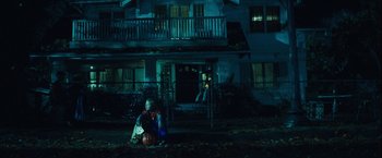 Movie still from “Halloween” (2007), directed by Rob Zombie – A person sitting on the ground in front of a house; Wide shot, High angle