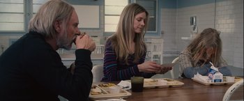 Movie still from “Halloween” (2007), directed by Rob Zombie – Two people sitting at a wooden table with plates of food; Medium shot, Over the shoulder angle