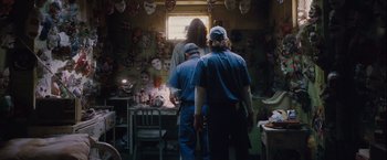 Movie still from “Halloween” (2007), directed by Rob Zombie – Two men in blue shirts and hats in front of a table with masks on the wall; Medium shot, Low angle