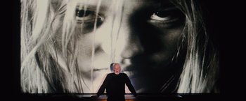 Movie still from “Halloween” (2007), directed by Rob Zombie – A man standing in front of a large picture of a woman's face; Medium shot, Low angle