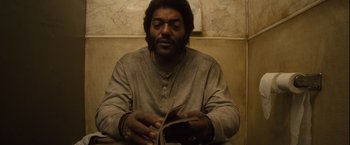 Movie still from “Halloween” (2007), directed by Rob Zombie – A man sitting in front of a wall holding a wallet; Close Up shot, High angle