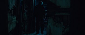 Movie still from “Halloween” (2007), directed by Rob Zombie – A man standing next to a door in a dark room; Medium shot, Low angle