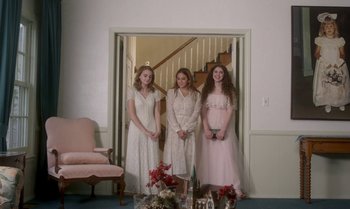 Movie still from “Ham on Rye” (2019), directed by Tyler Taormina – Three young women in white dresses standing in front of a chair; Wide shot, Low angle