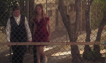 Movie still from “Ham on Rye” (2019), directed by Tyler Taormina – A woman in a red dress walking through a fence; Wide shot, Low angle