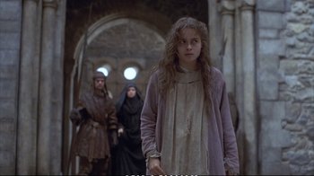 Movie still from “Hamlet” (1990), directed by Franco Zeffirelli – A young girl in a purple dress in front of two other people; Medium shot, Over the shoulder angle