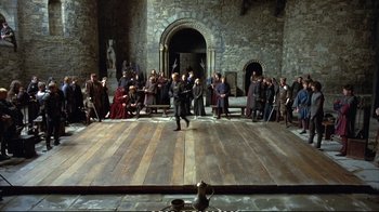 Movie still from “Hamlet” (1990), directed by Franco Zeffirelli – A group of people standing on a wooden stage; Extreme Wide shot, High angle
