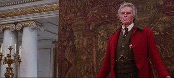 Movie still from “Hamlet” (1996), directed by Kenneth Branagh – An older man in a suit and tie standing in front of a wall; Medium shot, Low angle