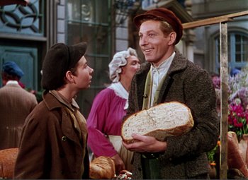 Movie still from “Hans Christian Andersen” (1952), directed by Charles Vidor – A man holding a loaf of bread in front of two other men; Medium shot, Over the shoulder angle