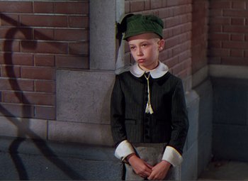 Movie still from “Hans Christian Andersen” (1952), directed by Charles Vidor – A young boy dressed as a leprechaun in front of a brick wall; Medium shot, High angle