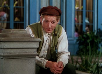 Movie still from “Hans Christian Andersen” (1952), directed by Charles Vidor – A man sitting on the side of a pillar wearing a hat; Medium shot, Low angle