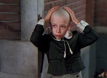 Movie still from “Hans Christian Andersen” (1952), directed by Charles Vidor – A young boy with a shaved head in front of a brick wall; Medium shot, High angle