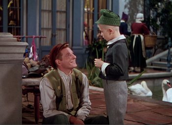 Movie still from “Hans Christian Andersen” (1952), directed by Charles Vidor – A man sitting next to a young boy in front of a building; Medium shot, High angle