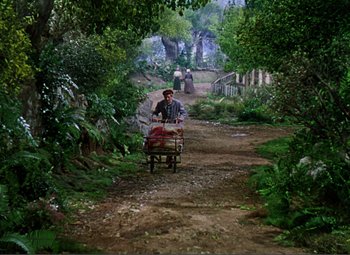 Movie still from “Hans Christian Andersen” (1952), directed by Charles Vidor – A man pushing a cart down a dirt road; Wide shot, High angle