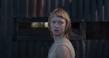 Movie still from “True History of the Kelly Gang” (2019), directed by Justin Kurzel – A young girl is standing in front of an old building; Close Up shot, Low angle