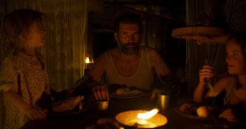 Movie still from “True History of the Kelly Gang” (2019), directed by Justin Kurzel – A man sitting at a table with a plate of food in front of him; Medium shot, Low angle