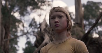 Movie still from “True History of the Kelly Gang” (2019), directed by Justin Kurzel – A young girl with blonde hair stands in front of a tree; Close Up shot, Low angle