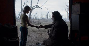 Movie still from “True History of the Kelly Gang” (2019), directed by Justin Kurzel – A woman holding a man's hand while sitting on the ground in a field; Medium shot, Over the shoulder angle