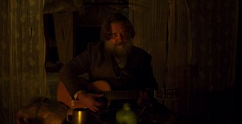 Movie still from “True History of the Kelly Gang” (2019), directed by Justin Kurzel – A man with a beard playing a guitar; Medium shot, Over the shoulder angle