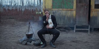 Movie still from “True History of the Kelly Gang” (2019), directed by Justin Kurzel – A man sitting on a chair holding a dog; Medium shot, Low angle