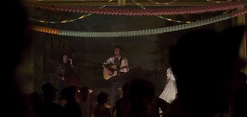 Movie still from “True History of the Kelly Gang” (2019), directed by Justin Kurzel – A man with a guitar in front of a group of people; Wide shot, Low angle