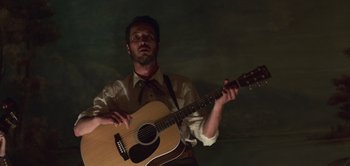 Movie still from “True History of the Kelly Gang” (2019), directed by Justin Kurzel – A man holding a guitar while wearing a tie; Medium shot, Low angle