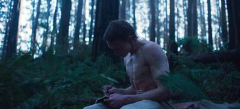 Movie still from “True History of the Kelly Gang” (2019), directed by Justin Kurzel – A man sitting in the woods writing on a piece of paper; Medium shot, Low angle
