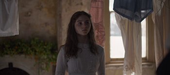 Movie still from “True History of the Kelly Gang” (2019), directed by Justin Kurzel – A woman in a white dress standing next to a window; Medium shot, Over the shoulder angle