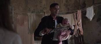 Movie still from “True History of the Kelly Gang” (2019), directed by Justin Kurzel – A man holding a baby holding a rifle; Medium shot, Low angle