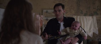 Movie still from “True History of the Kelly Gang” (2019), directed by Justin Kurzel – A young man holding a gun while holding a baby; Medium shot, Over the shoulder angle