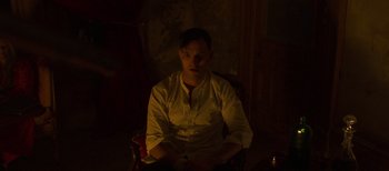 Movie still from “True History of the Kelly Gang” (2019), directed by Justin Kurzel – A man sitting in a chair in a dark room; Medium shot, High angle