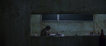 Movie still from “True History of the Kelly Gang” (2019), directed by Justin Kurzel – A man sitting at a table in a dark room; Wide shot, Overhead angle