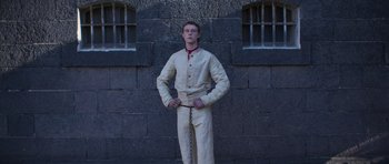 Movie still from “True History of the Kelly Gang” (2019), directed by Justin Kurzel – A man standing in front of a brick wall with chains; Medium shot, Low angle