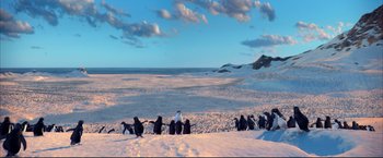 Movie still from “Happy Feet” (2006), directed by Warren Coleman – A group of penguins standing on top of a snow covered slope; Extreme Wide shot, High angle