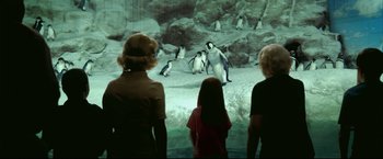 Movie still from “Happy Feet” (2006), directed by Warren Coleman – A group of people looking at penguins in an exhibit; Wide shot, High angle