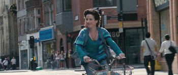 Movie still from “Happy-Go-Lucky” (2008), directed by Mike Leigh – A woman riding a bike down a street; Medium shot, Over the shoulder angle