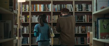 Movie still from “Happy-Go-Lucky” (2008), directed by Mike Leigh – A man and a woman standing in front of a book shelf; Medium shot, Over the shoulder angle