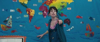 Movie still from “Happy-Go-Lucky” (2008), directed by Mike Leigh – A woman pointing to a map of the world on the wall; Medium shot, High angle