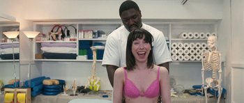 Movie still from “Happy-Go-Lucky” (2008), directed by Mike Leigh – A woman in a pink bra is being examined by a chiropractor; Medium shot, Over the shoulder angle