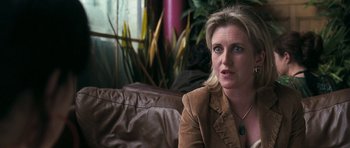 Movie still from “Happy-Go-Lucky” (2008), directed by Mike Leigh – A person sitting on a couch near a plant; Close Up shot, Over the shoulder angle