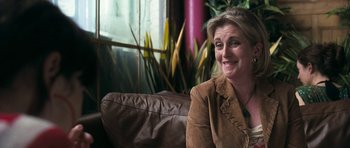 Movie still from “Happy-Go-Lucky” (2008), directed by Mike Leigh – A woman sitting on a couch in front of a window; Close Up shot, Over the shoulder angle