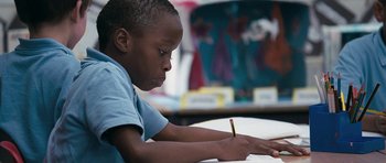 Movie still from “Happy-Go-Lucky” (2008), directed by Mike Leigh – A young boy writing on a piece of paper with a pencil; Close Up shot, High angle