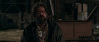 Movie still from “Happy-Go-Lucky” (2008), directed by Mike Leigh – A man with a beard is sitting in a dark room; Medium shot, Low angle