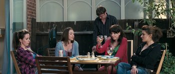 Movie still from “Happy-Go-Lucky” (2008), directed by Mike Leigh – A group of people sitting at a table with wine glasses; Medium shot, Over the shoulder angle