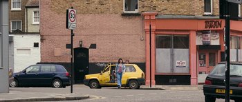 Movie still from “Happy-Go-Lucky” (2008), directed by Mike Leigh – A person standing next to a yellow car; Wide shot, Low angle