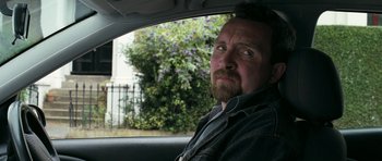 Movie still from “Happy-Go-Lucky” (2008), directed by Mike Leigh – A man sitting in the back seat of a car; Close Up shot, Over the shoulder angle